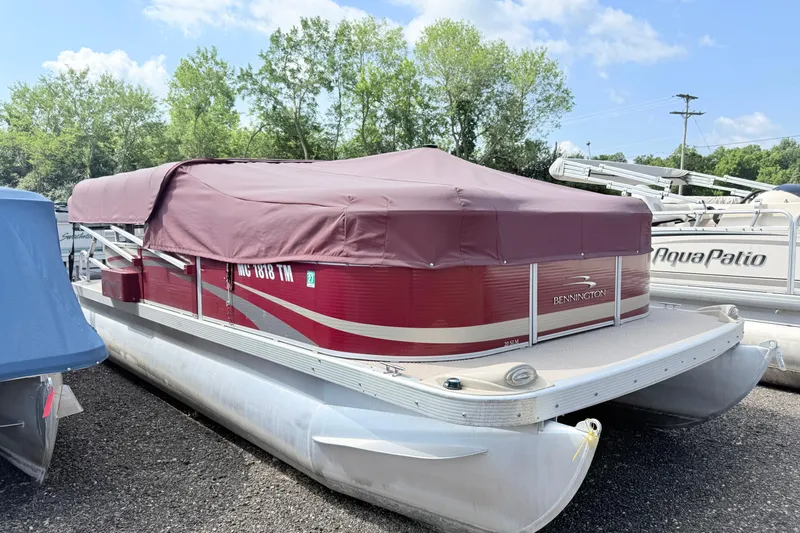 The Image of 2012 Bennington 20SLM pontoon boat with maroon cover, parked outdoors. - 1
