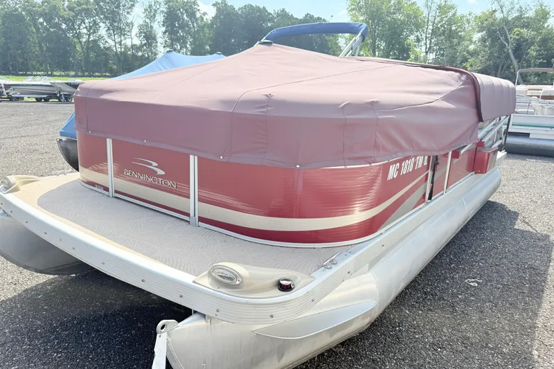 Slide: The Image of 2012 Bennington 20SLM pontoon boat with red cover, parked outdoors. - 2