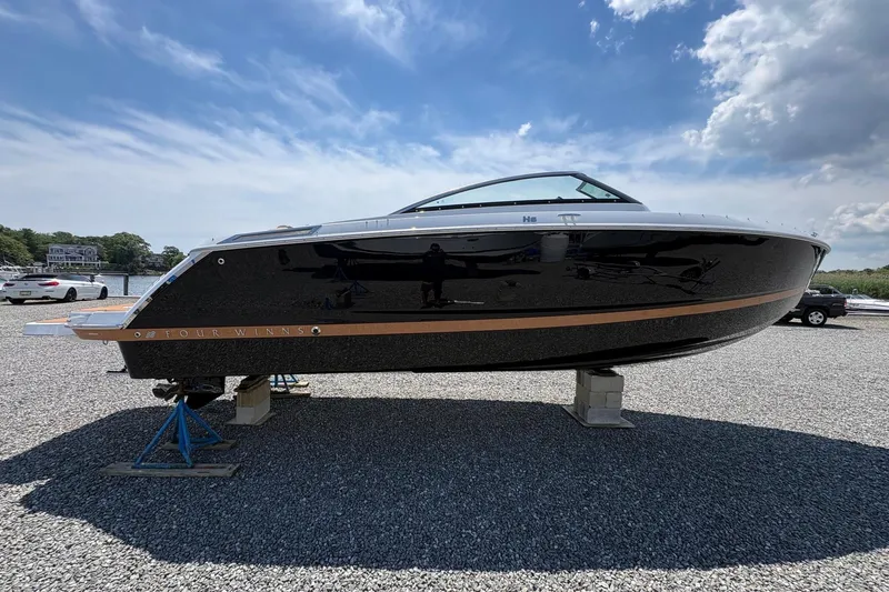 Slide: The Image of 2026 Four Winns H6 boat displayed on gravel lot under blue sky. - 2