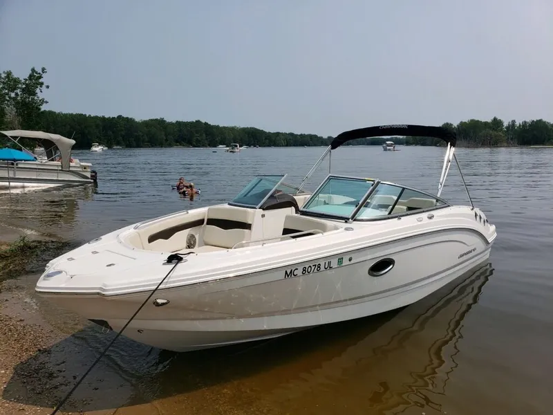 The Image of A white 2020 Chaparral 24 SSI boat is docked at the shore of a calm lake. - 0