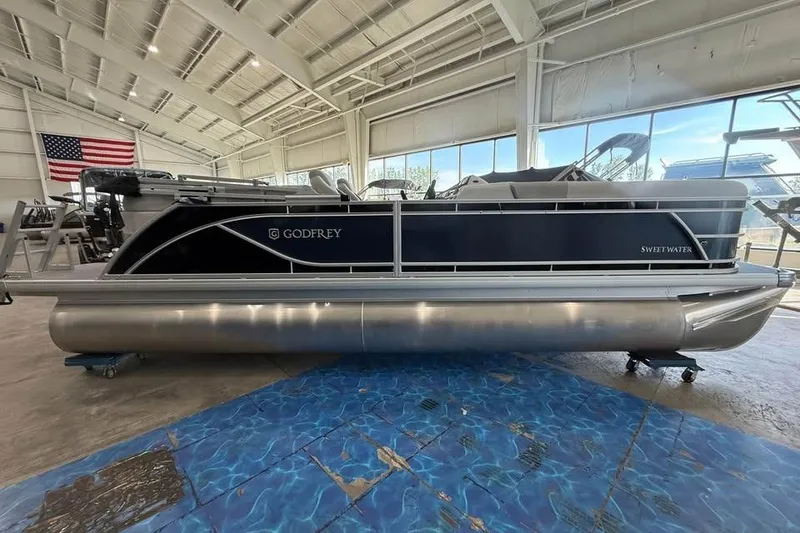 Slide: The Image of 2026 Godfrey Sweetwater 2286 SB pontoon boat in showroom with American flag backdrop. - 2