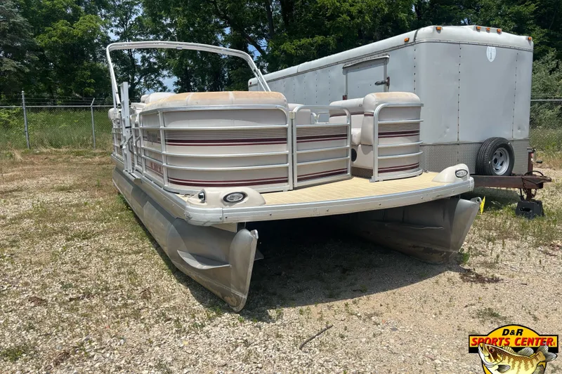 Slide: The Image of 2003 Sanpan 2200 LE pontoon boat parked on gravel near a trailer. - 2