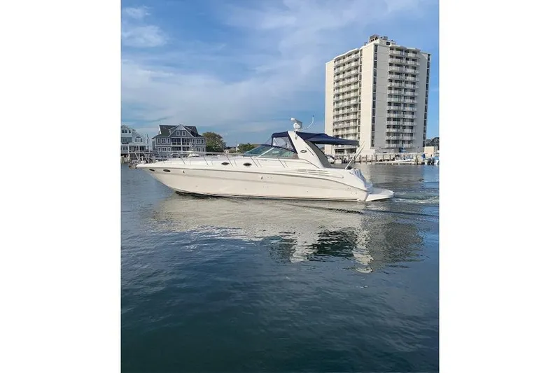 Slide: The Image of 1999 Sea Ray Sundancer 400 yacht cruising near waterfront buildings under a clear sky. - 2