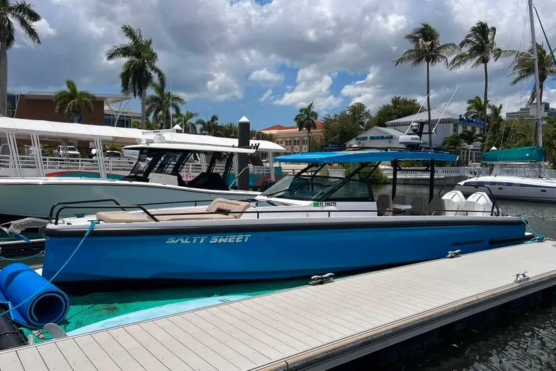Slide: The Image of 2023 Axopar Brabus 37 Sun-Top boat docked, blue hull, palm trees in background. - 8