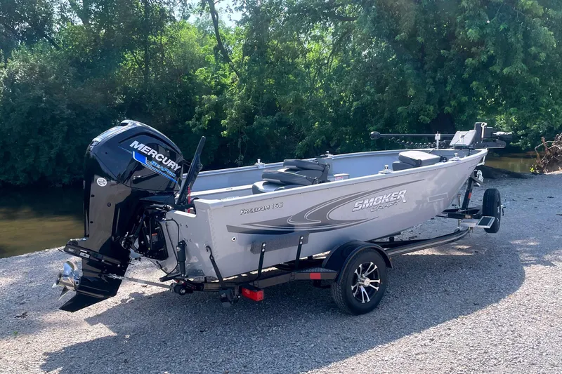 Slide: The Image of 2025 Smoker Craft Freedom 160 TL boat with Mercury engine on a trailer by a river. - 1