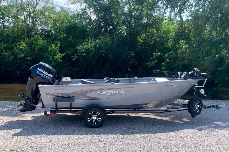 Slide: The Image of 2025 Smoker Craft Freedom 160 TL boat on trailer, parked near a riverbank. - 2
