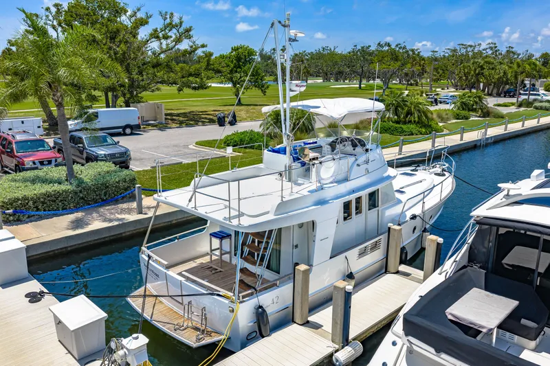 Slide: The Image of 2006 Beneteau Swift Trawler 42 docked at marina, surrounded by lush greenery and parked vehicles. - 11