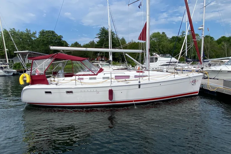 Slide: The Image of 2005 Hunter 38 sailboat docked in a marina, featuring red accents and canopy. - 1