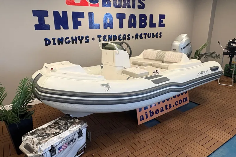 Slide: The Image of 2019 Caribe DL12 inflatable boat displayed indoors with Honda engine and promotional signage. - 2