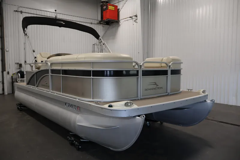 Slide: The Image of 2013 Bennington 20 SLMX pontoon boat in indoor storage, featuring sleek design and beige upholstery. - 2