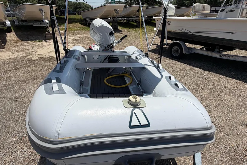Slide: The Image of 2022 Achilles inflatable boat with motor, parked on gravel, surrounded by other boats. - 1