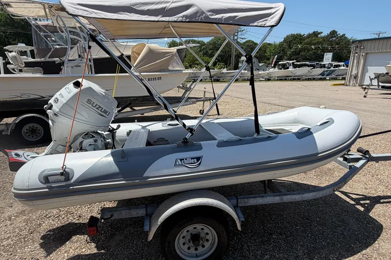 Slide: The Image of 2022 Achilles inflatable boat with Suzuki motor on a trailer, parked outdoors. - 2