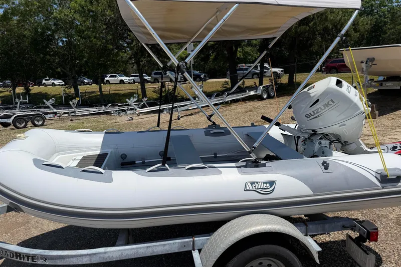 The Image of 2022 Achilles inflatable boat with Suzuki motor on trailer, parked outdoors. - 0