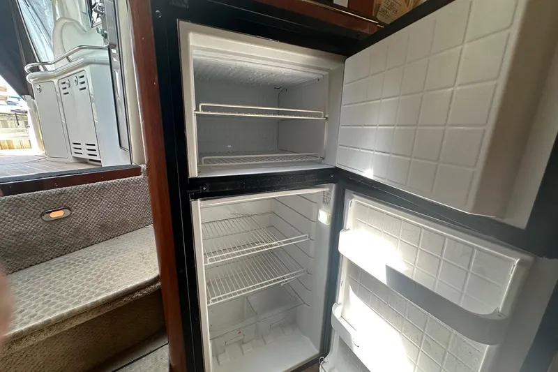 Slide: The Image of Open refrigerator inside 2001 Sea Ray 410 Sundancer yacht, showing empty shelves and steps nearby. - 10