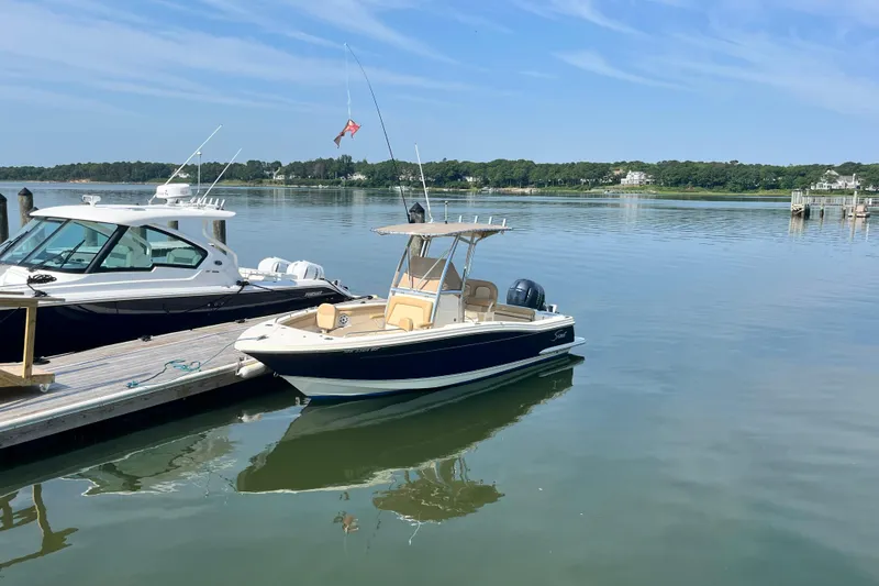 Slide: The Image of 2021 Scout 215 XSF boat docked on calm water under a clear blue sky. - 2