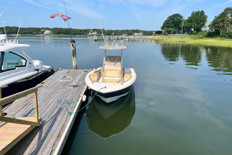 Slide: The Image of 2021 Scout 215 XSF boat docked on calm water, surrounded by scenic greenery. - 3