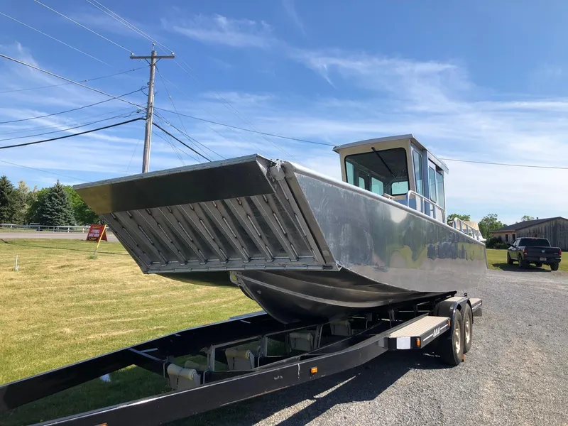 Slide: The Image of A 2026 Workboat Bayview Boats Landing Craft on a trailer, parked on a gravel path. - 2