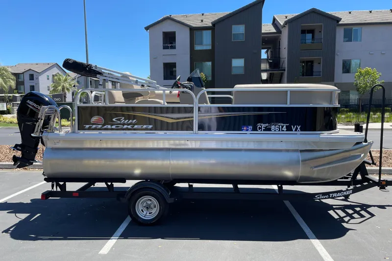 The Image of 2025 Sun Tracker Party Barge 16 DLX pontoon boat on trailer in parking lot. - 0