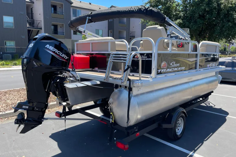 Slide: The Image of 2025 Sun Tracker Party Barge 16 DLX pontoon boat with Mercury engine, parked outdoors. - 2