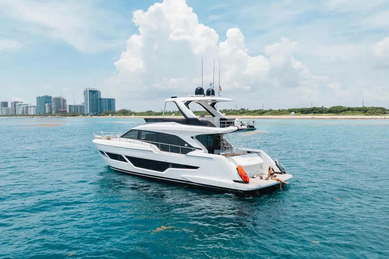 Slide: The Image of 2025 Ferretti Yachts 670 cruising on clear blue waters near a coastal cityscape. - 2