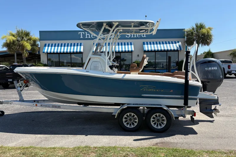 The Image of 2027 Pioneer 202 Islander boat on trailer, parked outside dealership with striped awnings. - 1