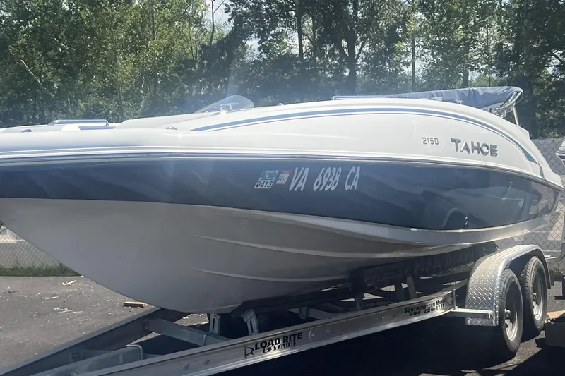 Slide: The Image of 2017 Tahoe 2150 boat on trailer, parked outdoors with trees in background. - 2