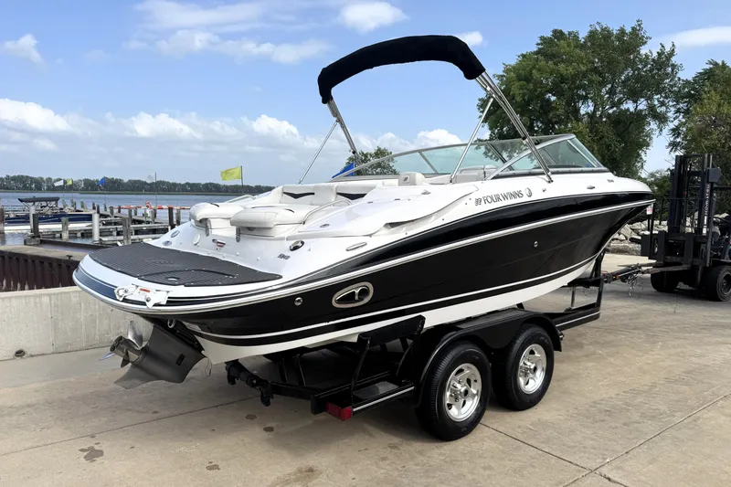 Slide: The Image of 2008 Four Winns H240 boat on trailer by lakeside, featuring sleek black and white design. - 5