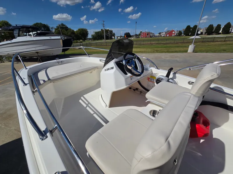 Slide: The Image of The image shows a 2027 Boston Whaler 130 Super Sport boat. It features white seating and a modern helm. Another boat and green landscape are visible in the background. - 9