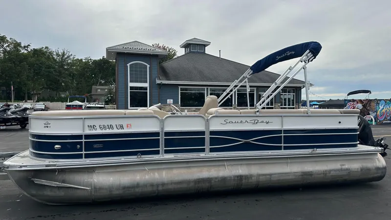 Slide: The Image of A 2018 South Bay S224CR pontoon boat is parked on a lot in front of a building. - 2