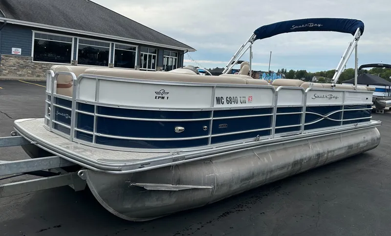 Slide: The Image of A 2018 South Bay S224CR pontoon boat on a trailer in front of a building. - 1