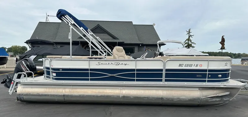 The Image of A 2018 South Bay S224CR pontoon boat with blue and white paint and a sunshade, parked on pavement. - 0