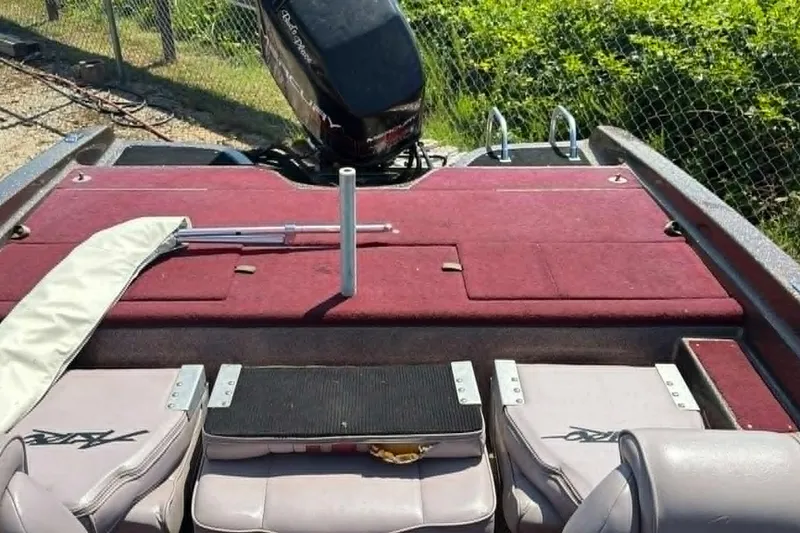 Slide: The Image of 1996 Astro 20fsx boat interior with red carpet and motor, parked near a fence. - 4