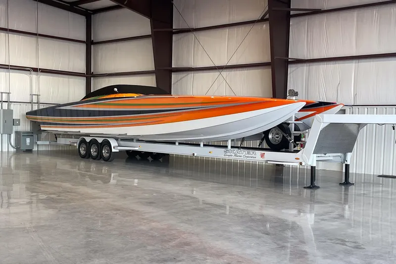 The Image of 2013 Skater 46 boat with vibrant orange and gray design on a trailer in a warehouse. - 0