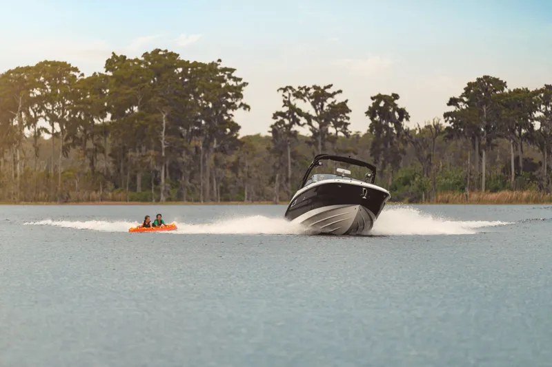 Slide: The Image of A 2026 Sea Ray SDX 270 towing an inflatable with two people across a calm lake. - 3