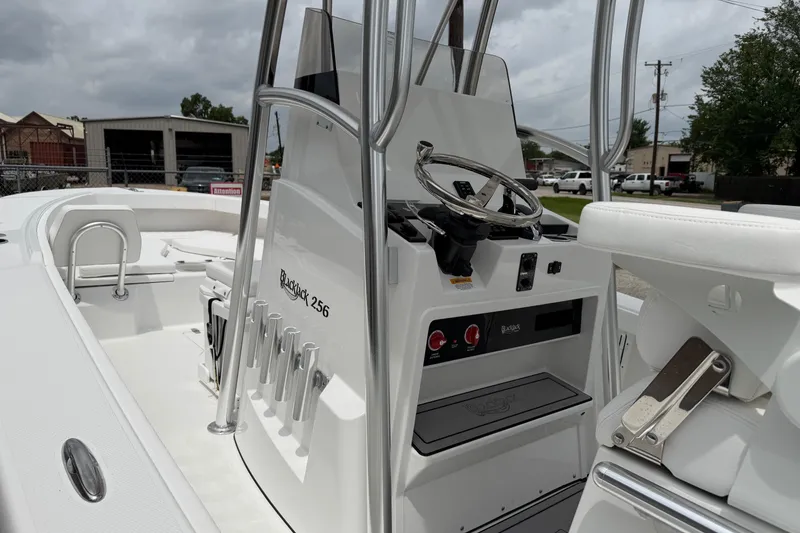 Slide: The Image of 2026 BlackJack 256 Coastal boat interior with steering console and seating, under cloudy skies. - 11