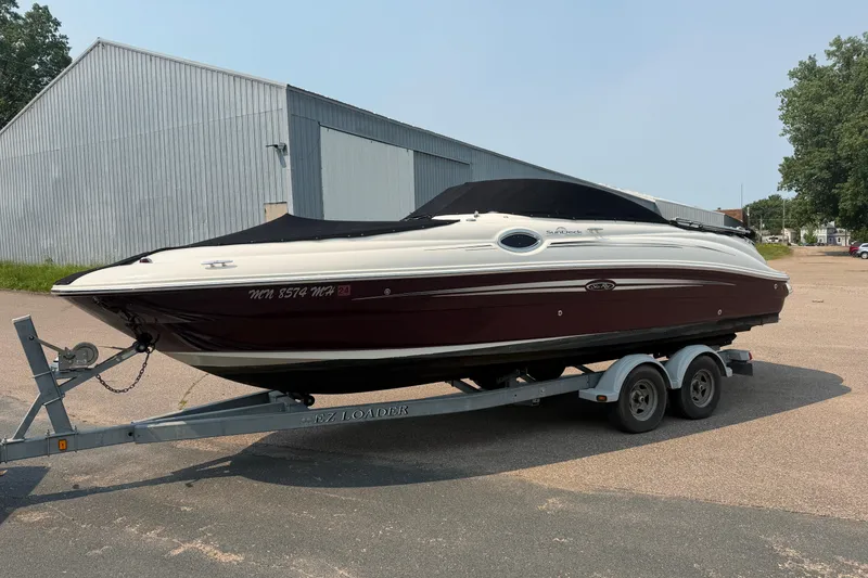 The Image of 2009 Sea Ray 240 Sundeck boat on trailer, parked near a metal building. - 0