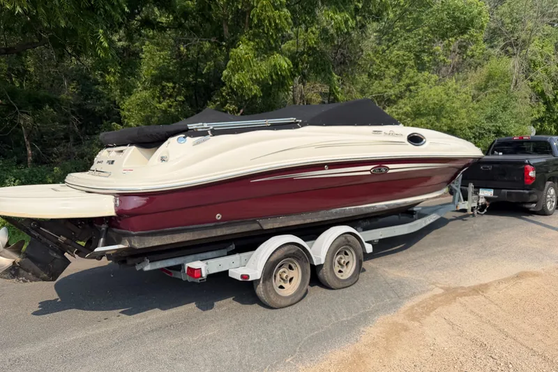 Slide: The Image of 2009 Sea Ray 240 Sundeck boat on trailer, parked near lush greenery. - 3