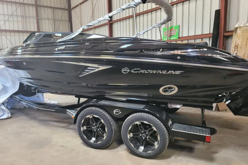 The Image of 2027 Crownline 220 SS LPX boat in a warehouse, sleek black design on trailer. - 1