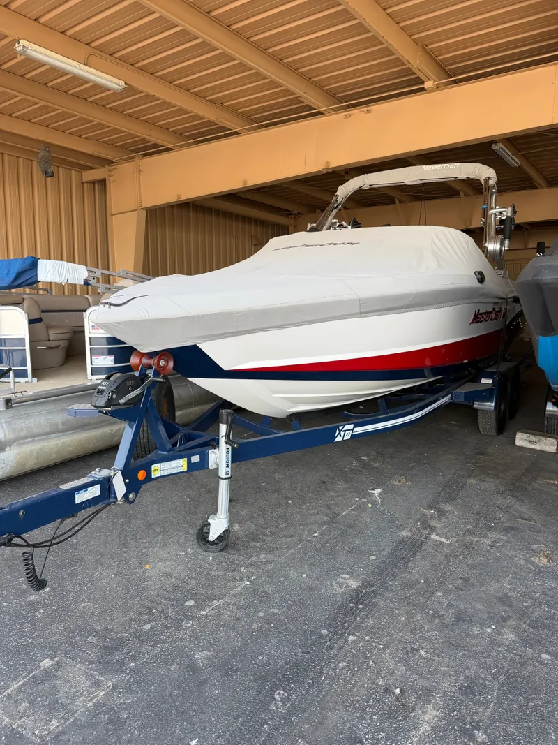 The Image of A 2018 MasterCraft XT23 boat on a trailer in a covered area. - 0