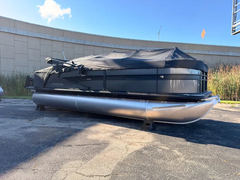 Slide: The Image of A 2027 Sylvan X3 LZ DH pontoon boat with a black cover, parked on a lot. - 1