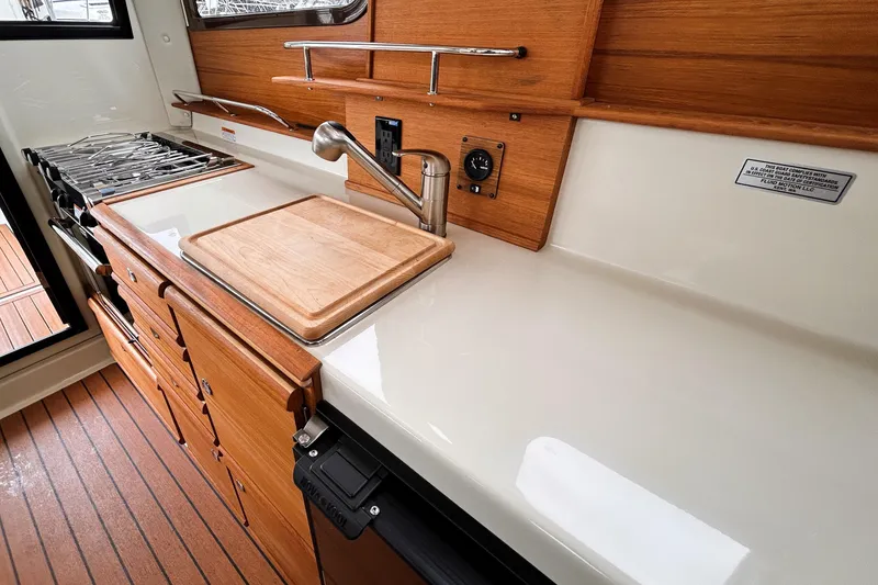 Slide: The Image of 2022 Ranger Tugs R-27 galley with wooden cabinetry, stove, and sink. - 8