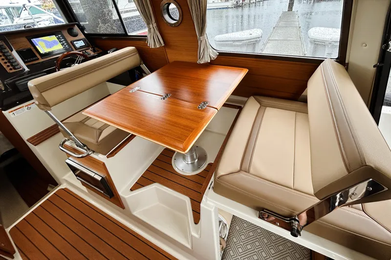 Slide: The Image of Interior of 2022 Ranger Tugs R-27 boat with wood table and beige seating. - 6