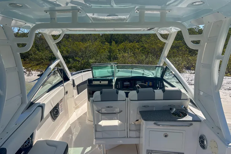 Slide: The Image of 2024 Chaparral 280 OSX boat interior with helm, seating, and dashboard, docked near a sandy shore. - 11