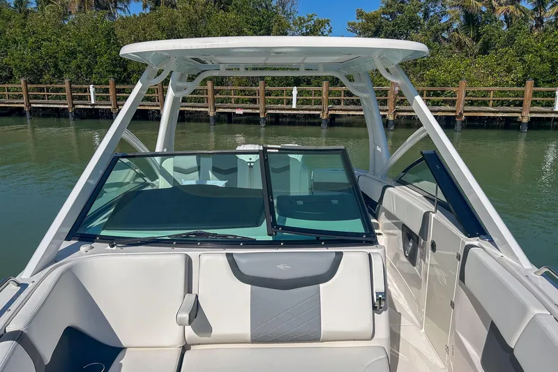 Slide: The Image of 2024 Chaparral 280 OSX boat interior with seating and windshield, docked by a wooden pier. - 4