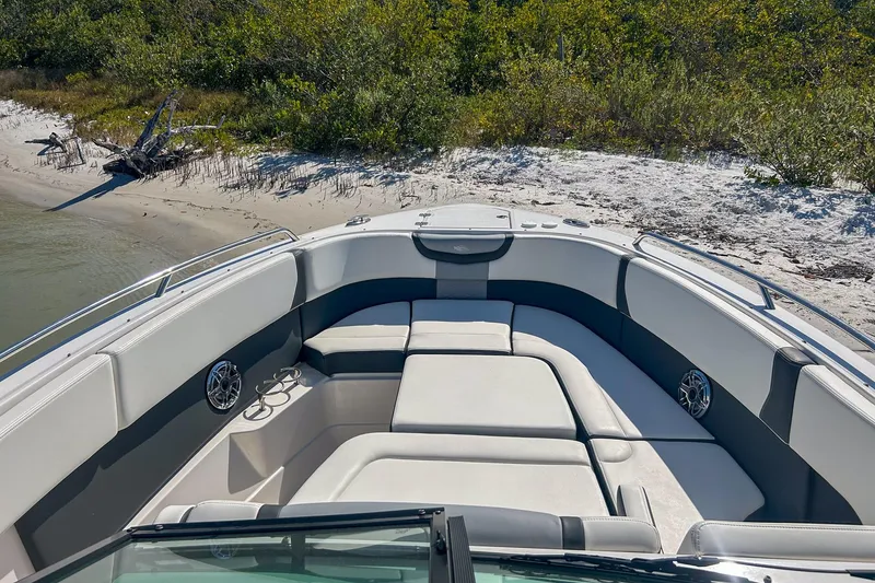 Slide: The Image of 2024 Chaparral 280 OSX boat interior with plush seating, docked on a sandy shore. - 6