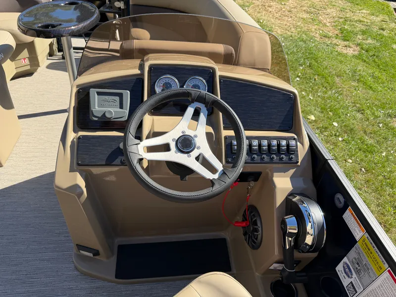 Slide: The Image of The image shows the helm of a 2027 Sylvan MIRAGE 822 CLZ DH. It features a modern design with a steering wheel, instrument gauges, and various controls. The flooring is carpeted, and part of the seating area is visible in the background. - 16