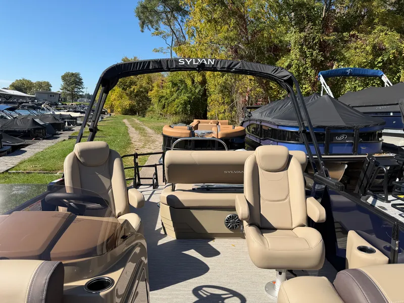 Slide: The Image of Sylvan MIRAGE 822 CLZ DH 2027 with beige seats and black bimini top, surrounded by trees. - 12