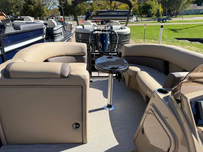 Slide: The Image of The image shows the interior of a Sylvan MIRAGE 822 CLZ DH pontoon boat with beige seating and a small table. - 14