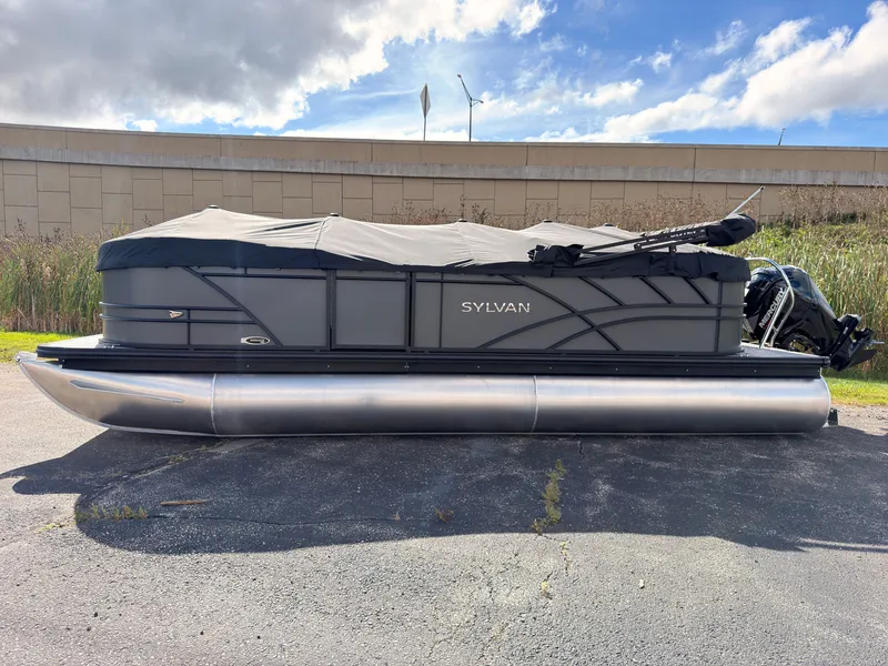 Slide: The Image of A 2027 Sylvan Mirage 822 LZ pontoon boat with a gray cover, parked on asphalt. - 1