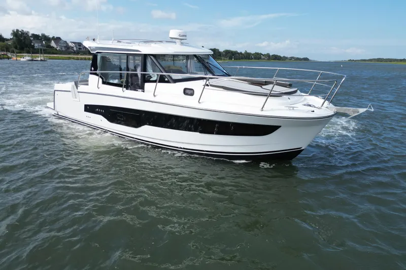 The Image of 2026 Jeanneau NC 1095 Coupe cruising on a calm waterway under a clear blue sky. - 0